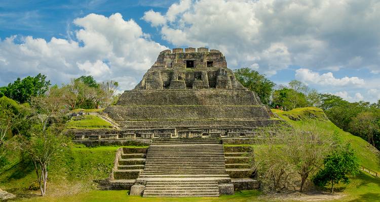 Une grande structure de temple maya ancien avec des marches en pierre et un environnement verdoyant.