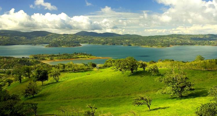Lush green hills surround Lake Arenal under bright clouds in Costa Rica.