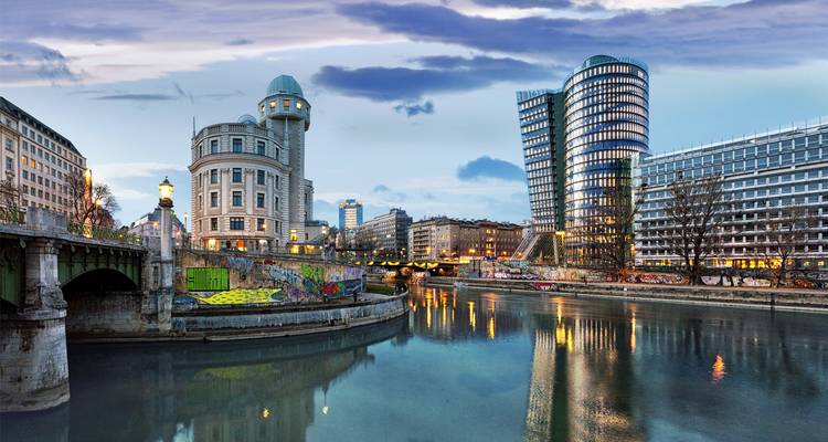 Escena urbana en Viena con edificios modernos e históricos en la ribera de un río.