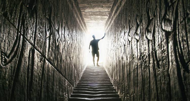 Silueta de una persona de pie en la entrada de un túnel con jeroglíficos.