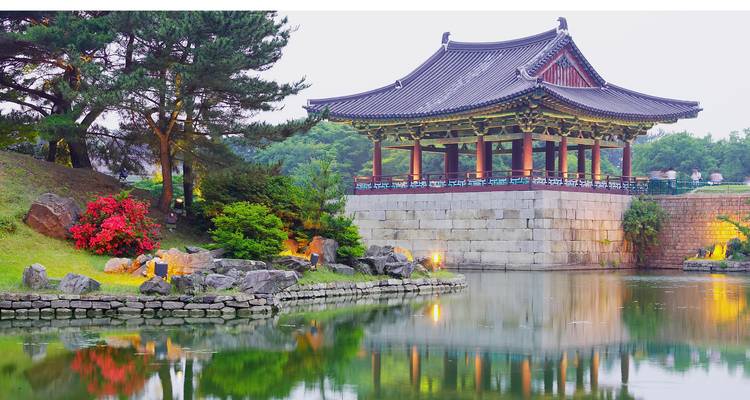 Pabellón coreano tradicional junto a un estanque con flora vibrante.