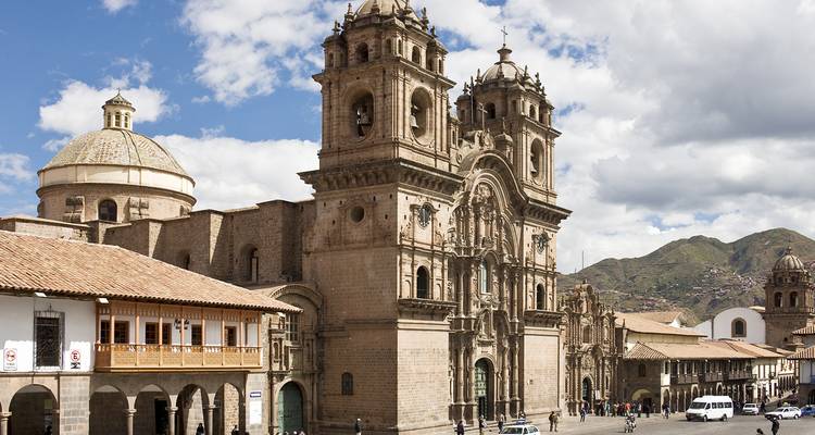 Historic church and buildings in a city square with mountains nearby.