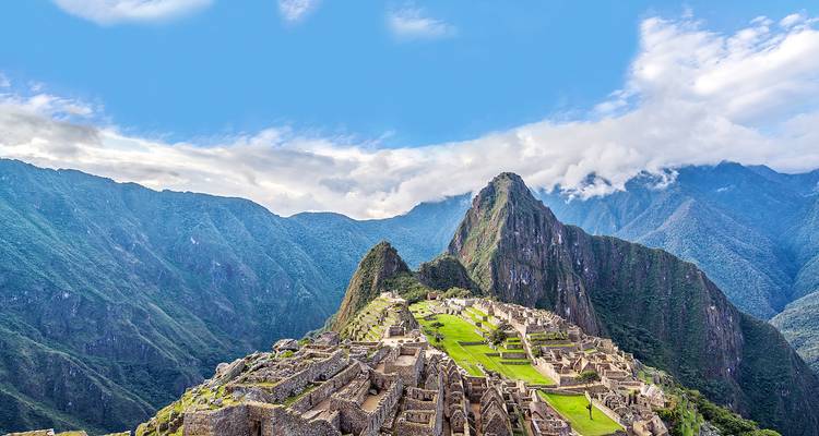 Vue aérienne du Machu Picchu avec son arrière-plan montagneux emblématique et un ciel nuageux.