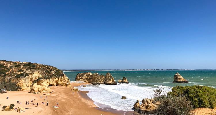 Plage de sable avec formations rocheuses et vagues.