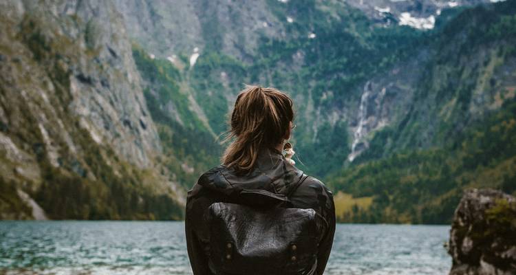 Wanderer mit Rucksack blickt auf einen von Bergen umgebenen See.