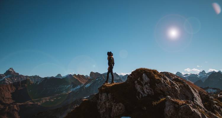 Silhouette eines Wanderers auf einem Berggipfel unter blauem Himmel.