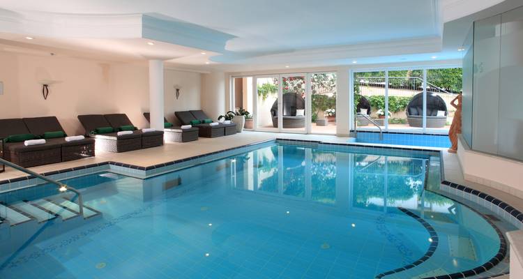Piscina cubierta en un hotel con una persona relajándose junto a la ventana.