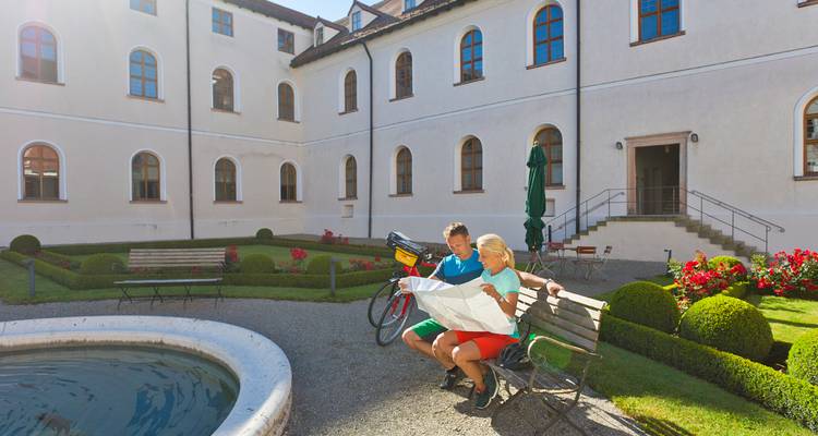 Fietsers die op een bankje zitten en een papieren kaart bestuderen in een verzorgde binnenplaats