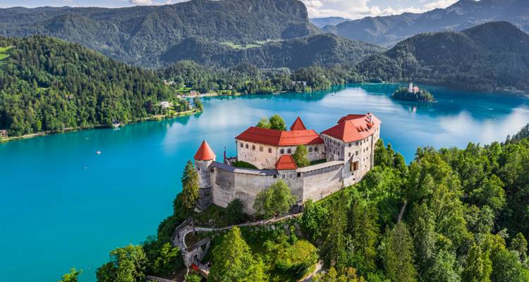Vista aérea de un castillo junto al lago Bled con un impresionante telón de fondo montañoso.