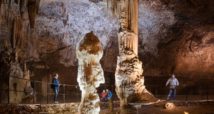 Turistas explorando dentro de una gran cueva con estalactitas y estalagmitas.