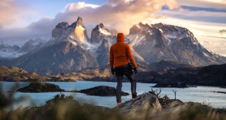 Personne debout sur un point de vue rocheux avec des montagnes spectaculaires et un lac.