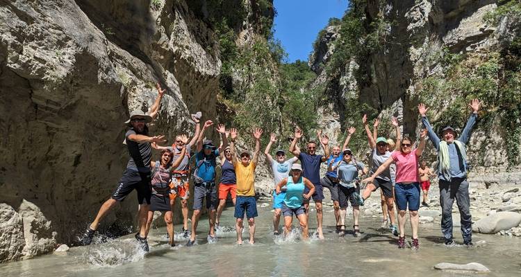 Grupo de personas saltando en un río poco profundo rodeado de acantilados rocosos.