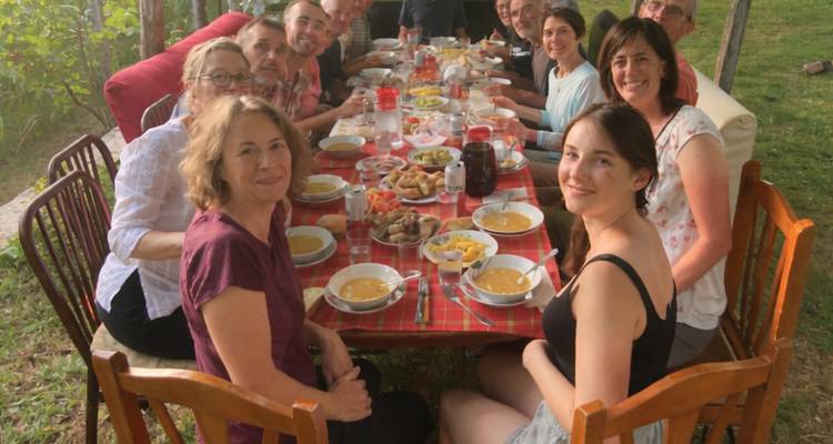 Grupo de personas disfrutando de una comida en una mesa larga al aire libre.