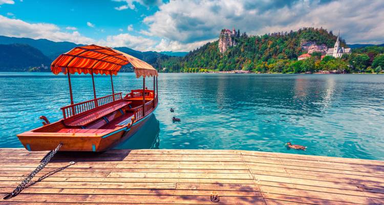 Barco de madera amarrado en un muelle con un lago pintoresco y montañas de fondo.