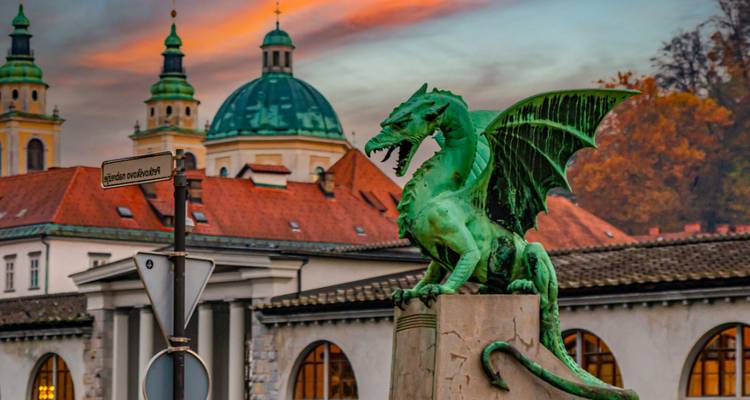 Estatua de un dragón frente a edificios históricos contra un cielo colorido.