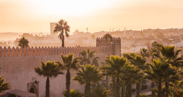 Eine Stadtansicht mit einer historischen Festung und Palmen bei Sonnenuntergang.