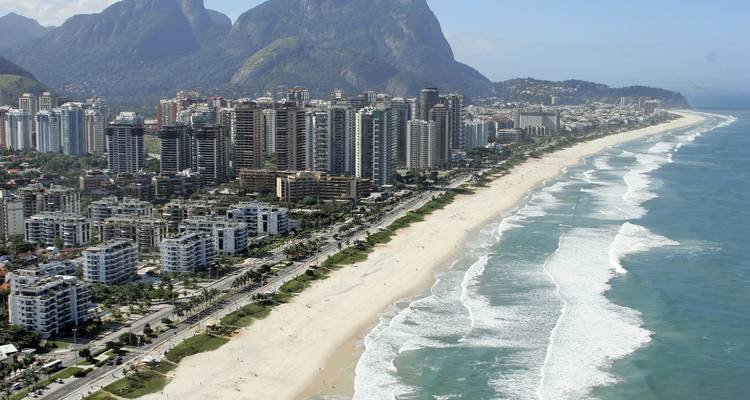 Luchtfoto van een lang zandstrand met golven en stadshorizon.