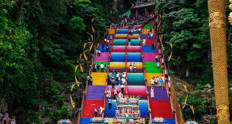 Des centaines de visiteurs gravissent les escaliers arc-en-ciel vibrants des grottes de Batu sous une canopée luxuriante.