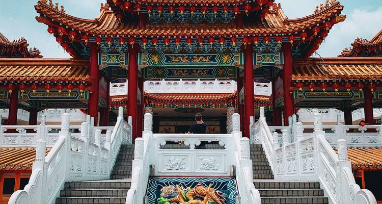 Un voyageur se tient à l'entrée ornée du temple Thean Hou avec une décoration complexe rouge et dorée.