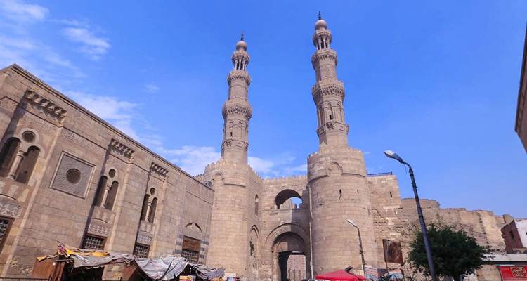 Puerta de entrada histórica flanqueada por dos minaretes contra un cielo azul.