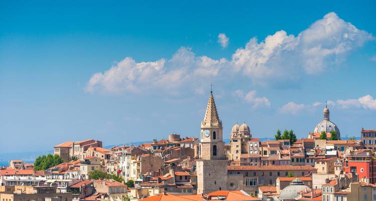 Des toits en terre cuite et un clocher d'église parsèment l'horizon du quartier historique de Marseille sous un ciel bleu dégagé.