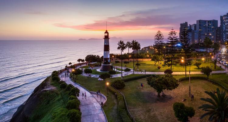 Phare au bord de l'océan au coucher du soleil avec des gens qui se promènent à proximité.