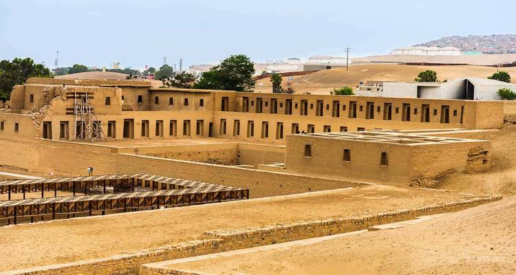 Ruines anciennes avec un environnement sablonneux et des bâtiments en arrière-plan.