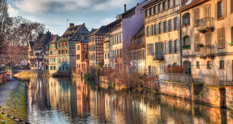 Malerische Fachwerkhäuser der Straßburger Petite France spiegeln sich in einem ruhigen Kanal unter warmem Morgenlicht wider.