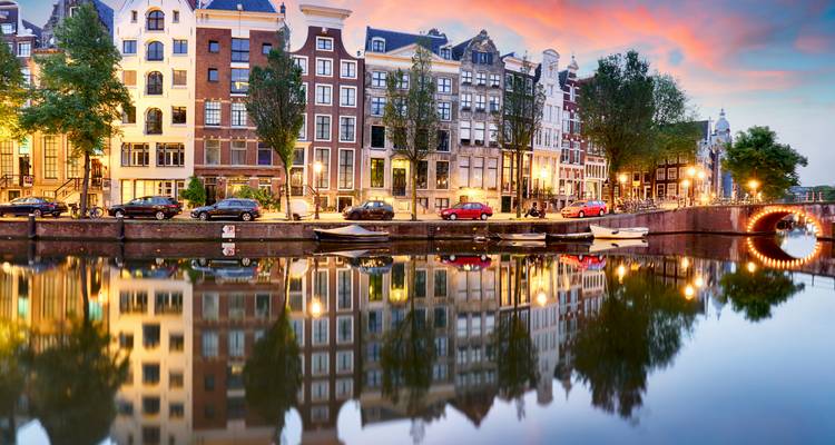 Canal de Ámsterdam con edificios reflejados en el agua al atardecer.