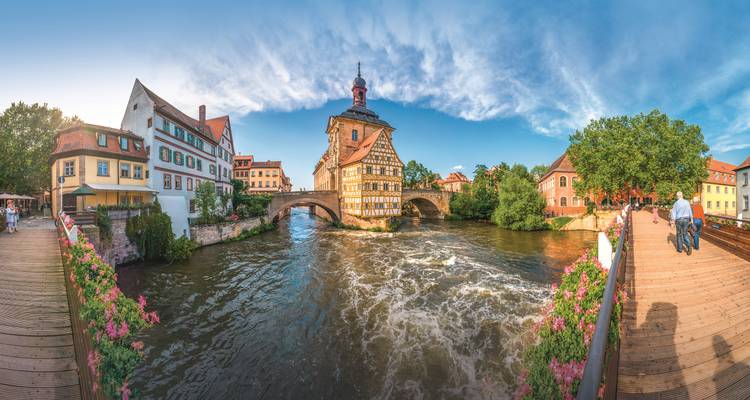 Weitblick auf Bambergs Altes Rathaus, das den Fluss überspannt, mit lebendigen Himmeln und blumengesäumten Brücken.