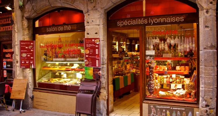 Une devanture accueillante d'épicerie fine lyonnaise présentant des pâtisseries locales et de la charcuterie.
