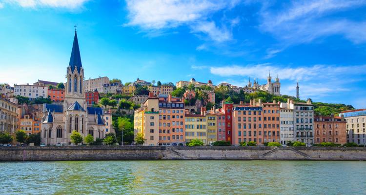 Bâtiments colorés au bord de la rivière et clocher d'église le long de la Saône à Lyon sous un ciel bleu éclatant.