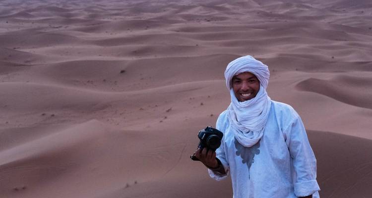 Personne en vêtements traditionnels tenant un appareil photo dans un paysage désertique.