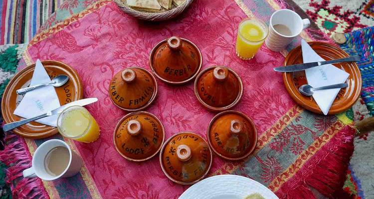 Configuration de petit-déjeuner marocain traditionnel avec des tagines et des boissons sur une table colorée.