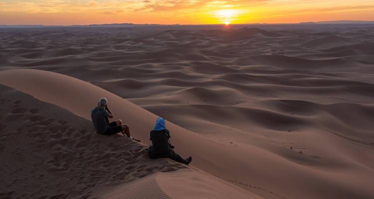 Deux personnes assises sur des dunes observant le lever du soleil dans le désert.
