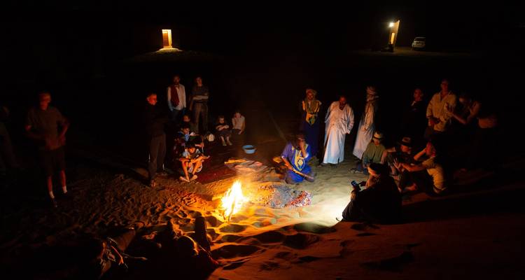 Un grand groupe rassemblé autour d'un feu de camp la nuit dans le désert.