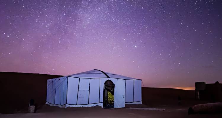 Personne debout à l'extérieur d'une tente blanche sous un ciel nocturne étoilé.