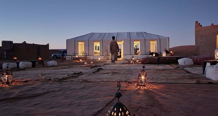Personne marchant vers un camp de tentes de luxe au crépuscule.
