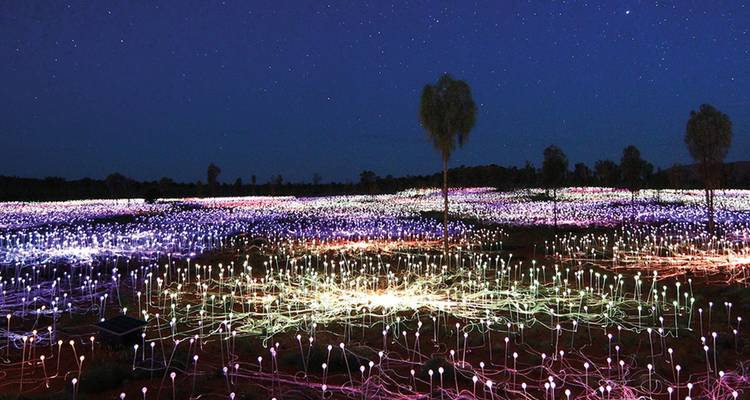 Instalación artística nocturna Field of Light cerca de Uluru, con miles de tallos luminosos bajo un cielo estrellado.