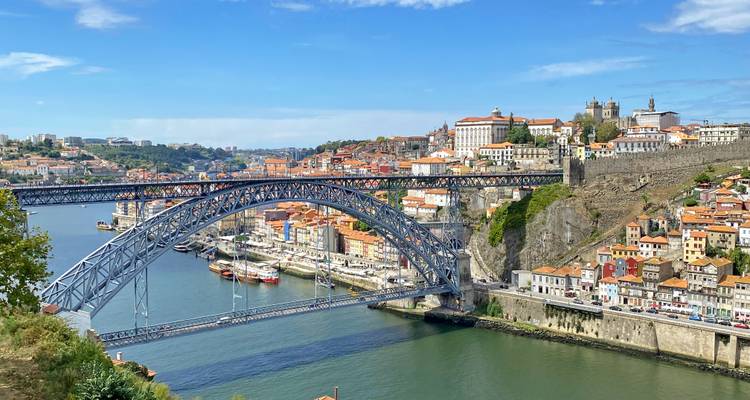 Vista panorámica del Puente Dom Luís I arqueándose sobre el río Douro con edificios de Porto de tejados rojos en ambas orillas.