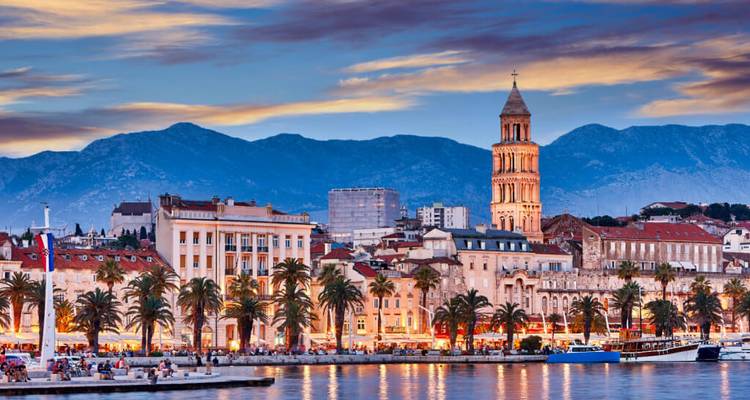 Ville côtière avec architecture historique et toile de fond montagneuse au crépuscule.