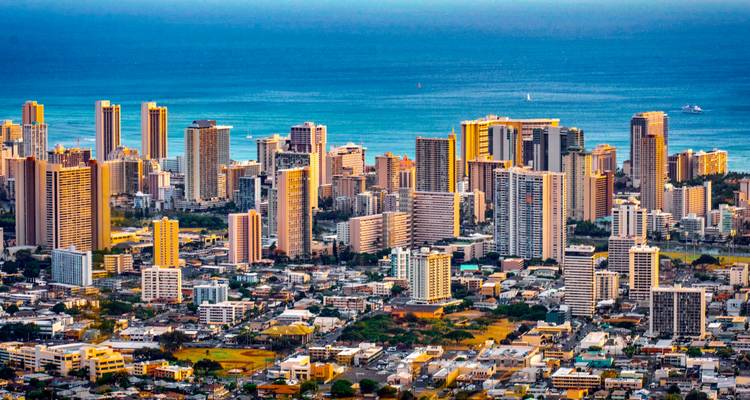 Luchtfoto van de skyline van Honolulu omlijst door turquoise oceaan en diepblauwe horizon.