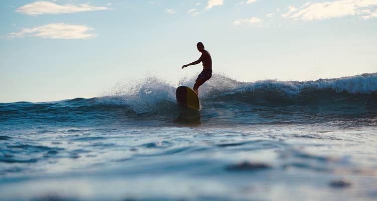 Silhouet van een surfer die snijdt op een golf met waterdruppels die spatten in het schemerlicht.