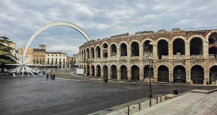 Les anciennes arches de pierre des Arènes de Vérone dominent une place urbaine nuageuse avec une sculpture d'étoile moderne.