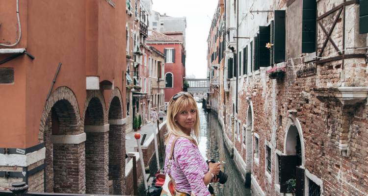 Un voyageur regarde en arrière le long d'un étroit canal vénitien bordé de palais en briques anciennes.