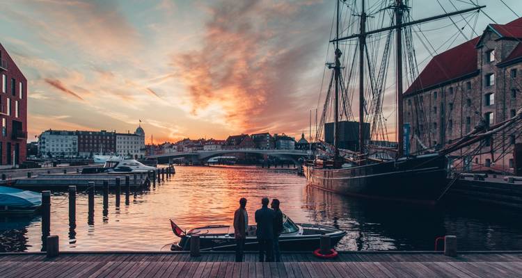 Personas admirando un atardecer junto al puerto con barcos atracados.