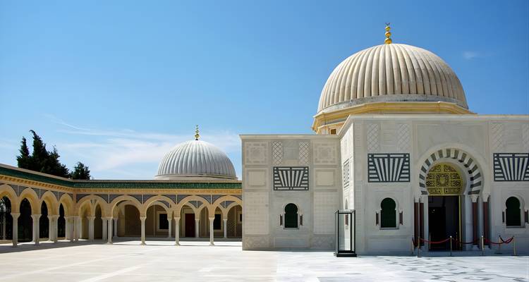 Eine Moschee mit weißen Kuppeln und Bögen an einem sonnigen Tag.