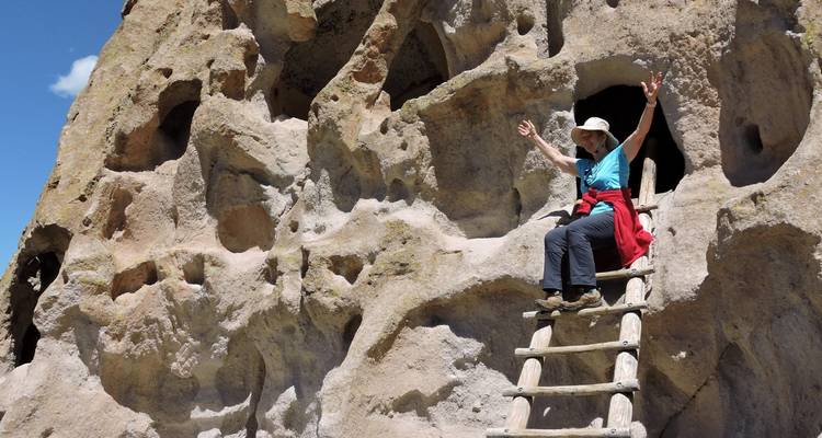 Una persona subiendo una escalera de madera apoyada contra una pared rocosa erosionada con agujeros.