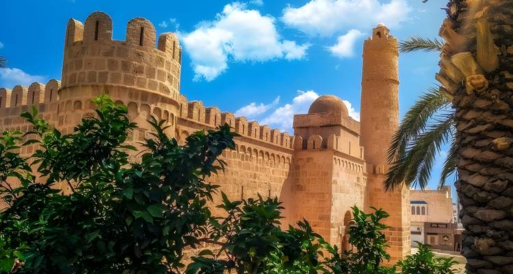Una antigua fortaleza con grandes muros de piedra y una torre bajo un cielo azul.
