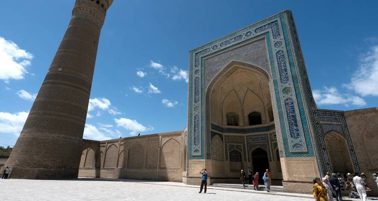 Touristen erkunden den großartigen gekachelten Eingang und das aufragende Minarett einer historischen Moschee unter blauem Himmel.